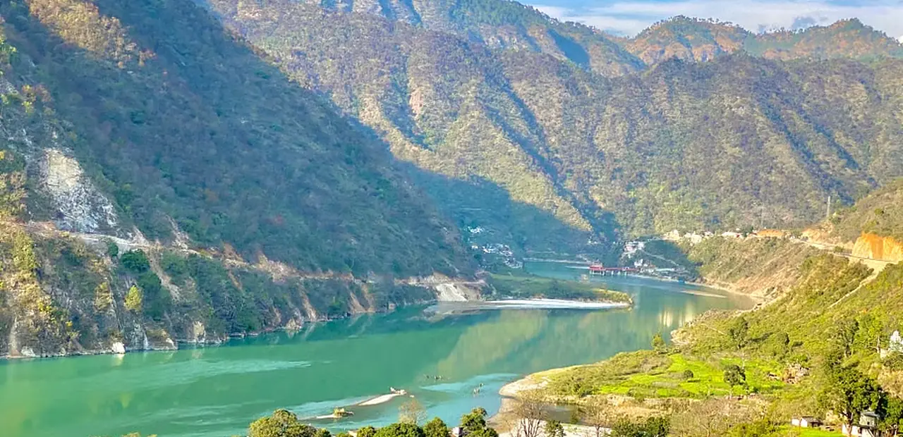 A highway cut into the hillside above a turquoise Himalayan river in Uttarakhand